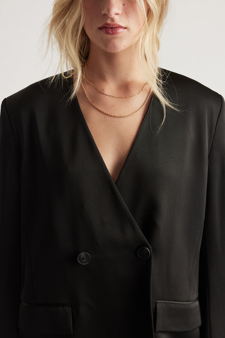 Close-up of a woman wearing layered delicate gold chains over a sleek black blazer with a deep V neckline