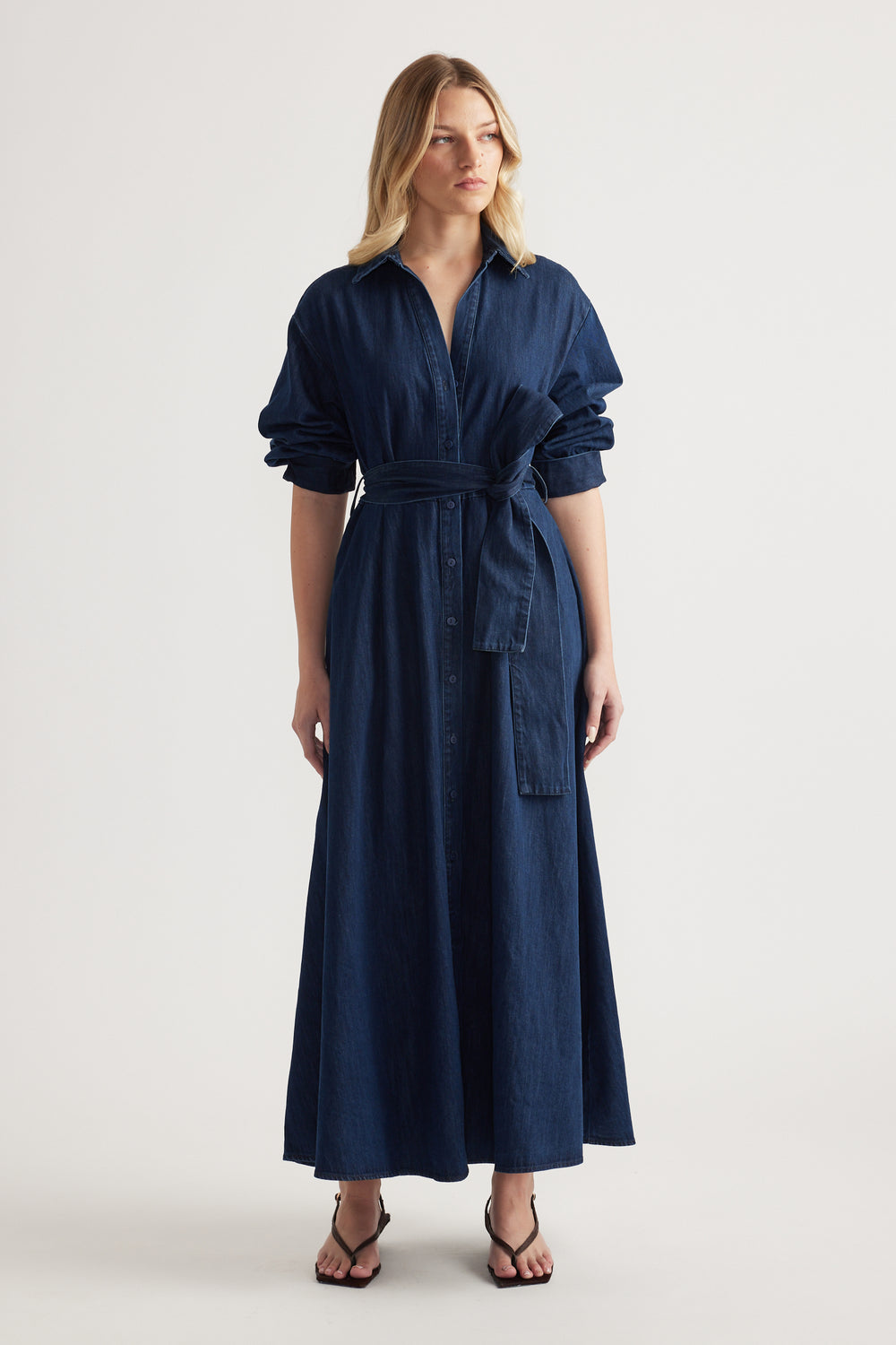 Woman in a dark denim midi shirt dress with rolled sleeves, collar and adjustable waist tie