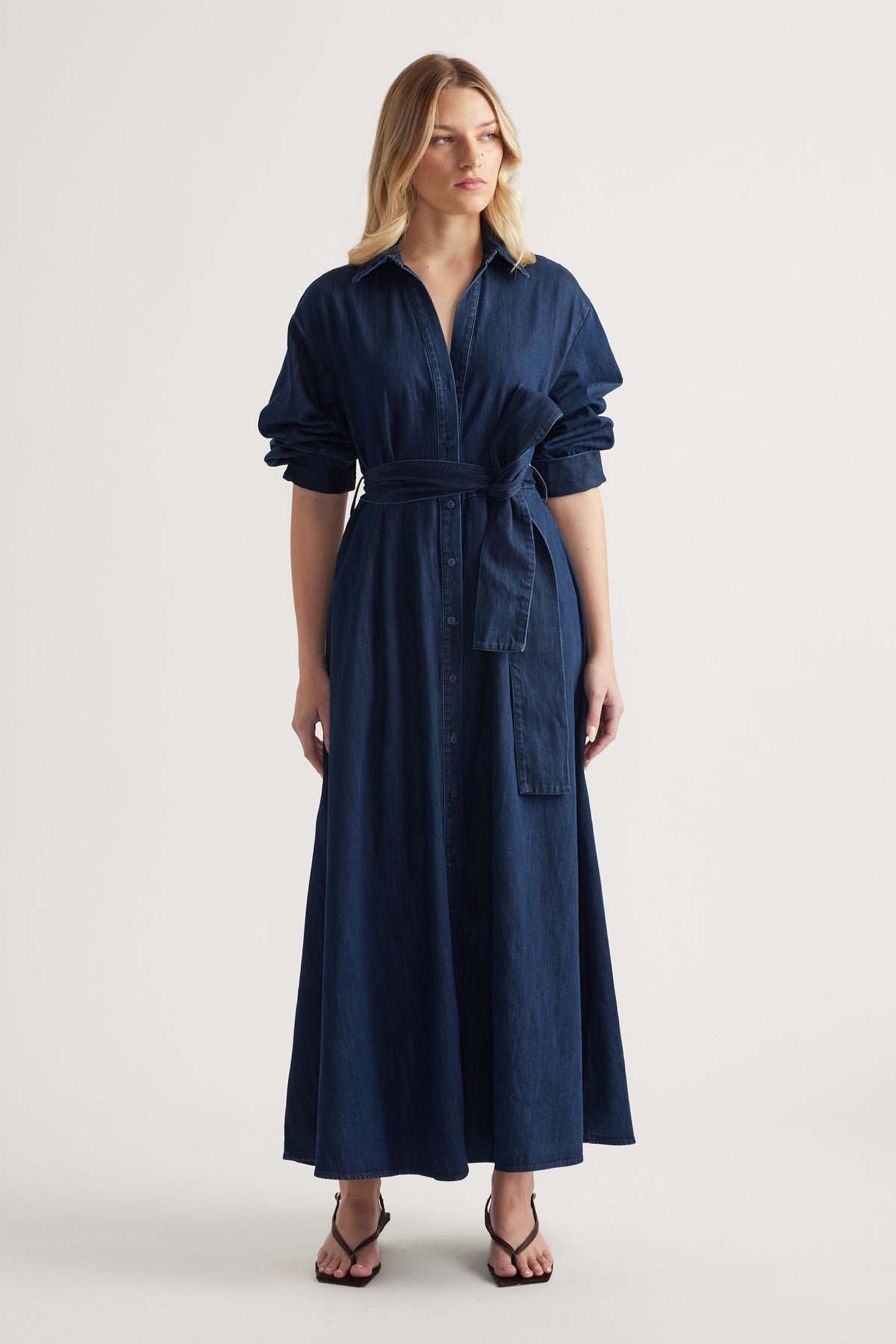 Woman in a dark denim midi shirt dress with rolled sleeves, collar and adjustable waist tie