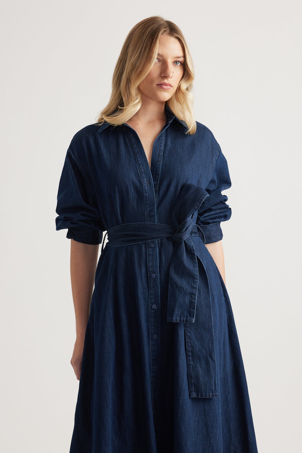 Woman wearing a navy denim midi shirt dress with a collared neckline, rolled sleeves and adjustable waist tie
