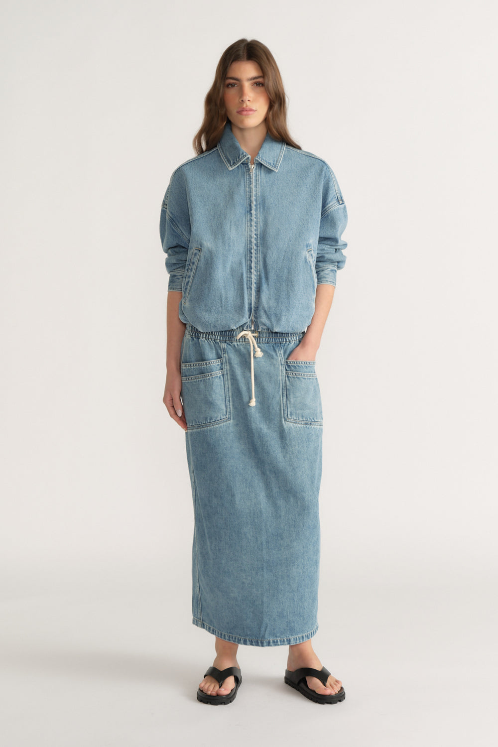 Woman wearing a denim midi skirt with a matching denim jacket and black sandals