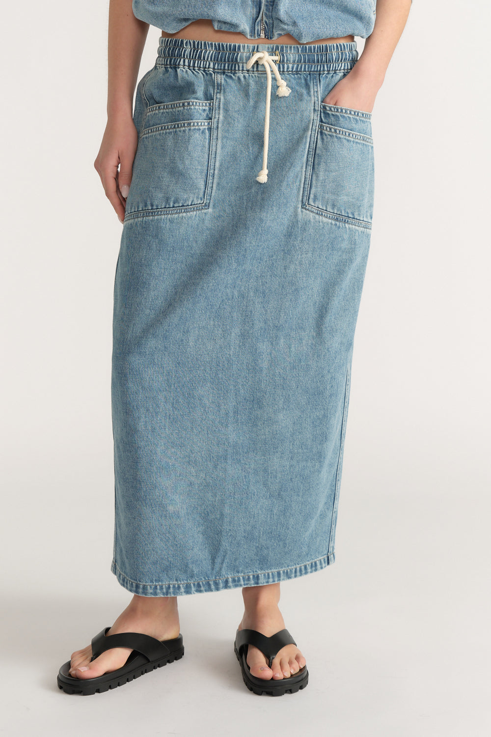 Model wearing a light wash denim midi skirt with an elastic drawstring waist and front patch pockets
