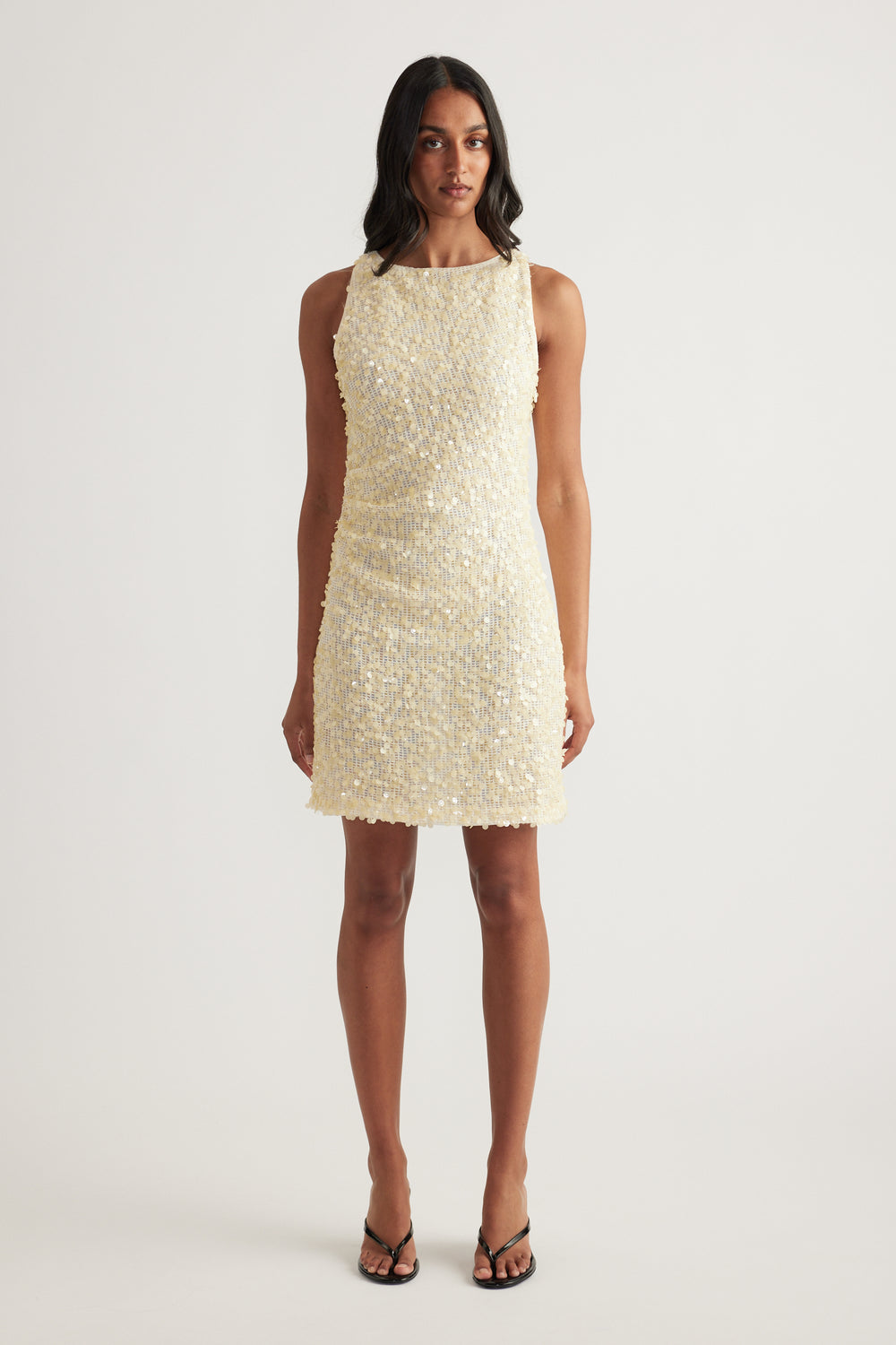 Woman wearing a cream sequin mini dress with a sleeveless cut, boat neckline and fitted silhouette