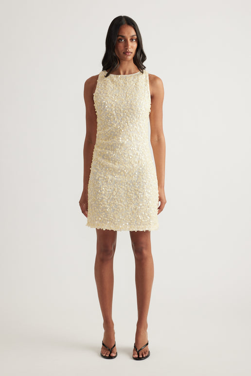 Woman wearing a cream sequin mini dress with a sleeveless cut, boat neckline and fitted silhouette