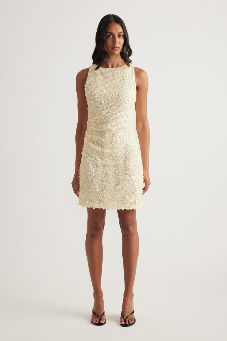 Woman wearing a cream sequin mini dress with a sleeveless cut, boat neckline and fitted silhouette