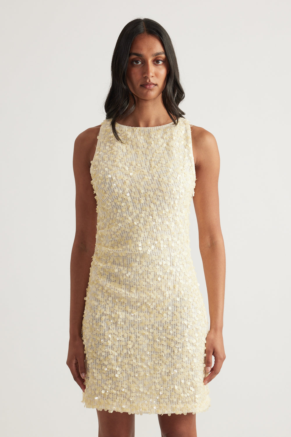 Model wearing a cream sequin mini dress with a sleeveless boat neckline, scoop back and fitted silhouette