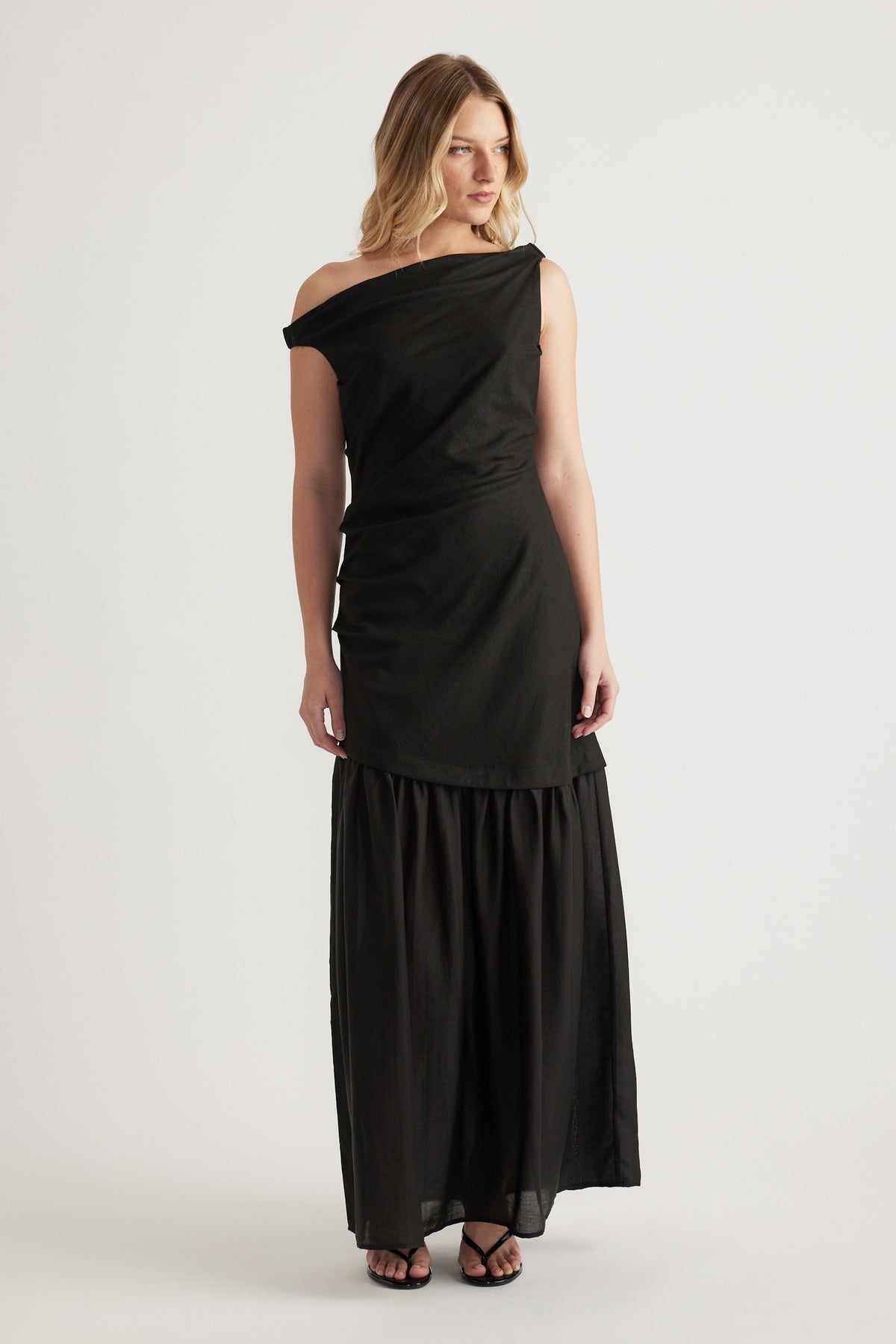 Woman wearing a black off shoulder spliced maxi dress with a draped bodice and flowing skirt