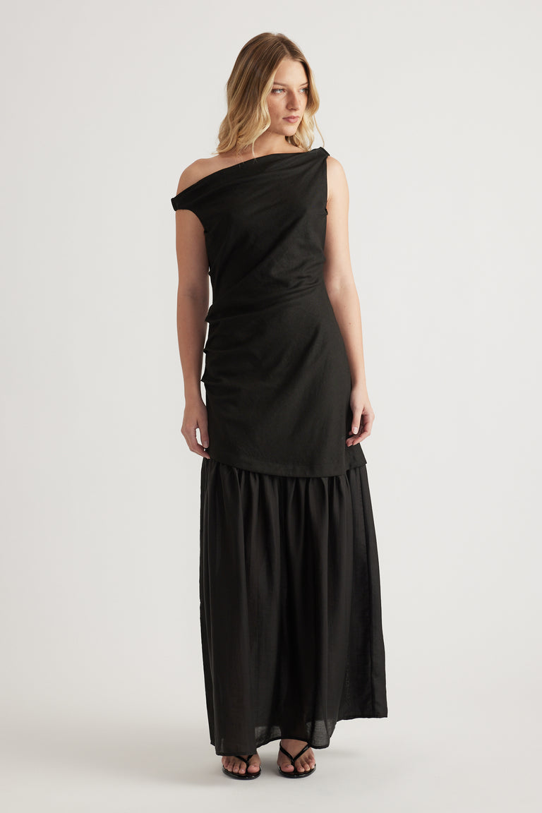 Woman wearing a black off shoulder spliced maxi dress with a draped bodice and flowing skirt