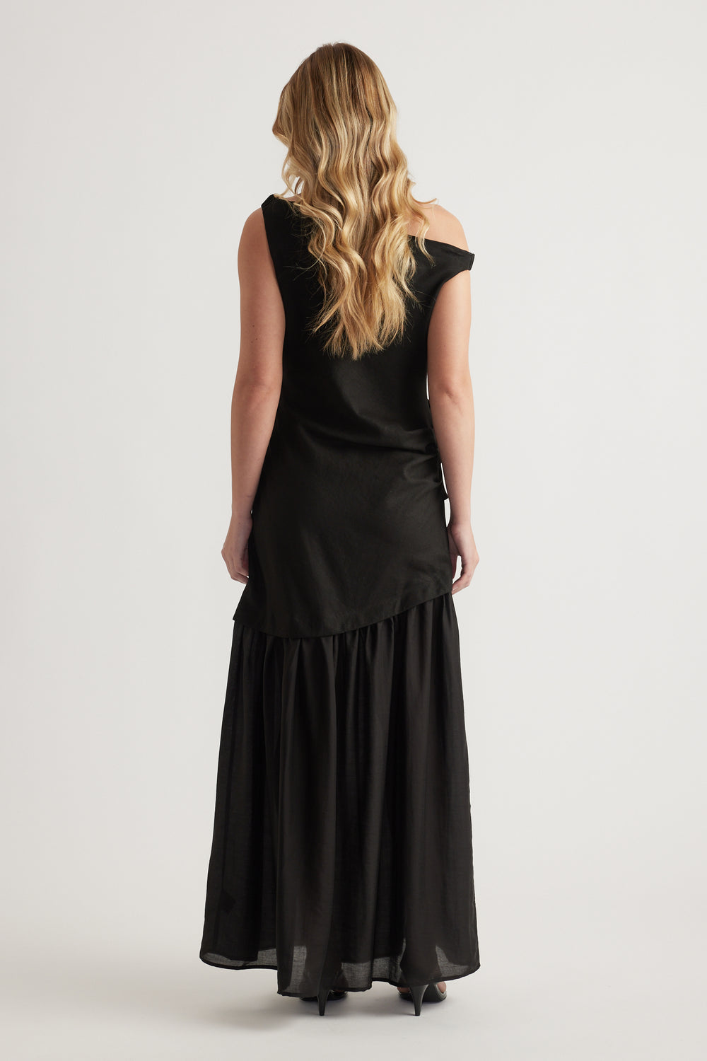 Woman wearing a black off shoulder maxi dress with a flowing A line skirt from behind