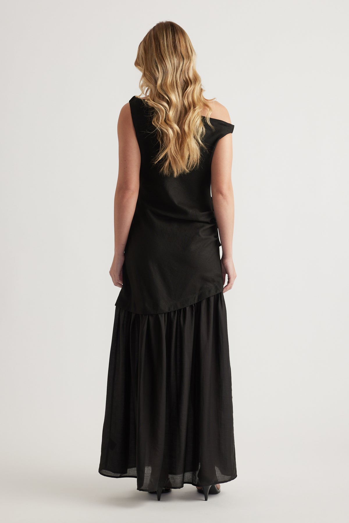 Woman wearing a black off shoulder maxi dress with a flowing A line skirt from behind