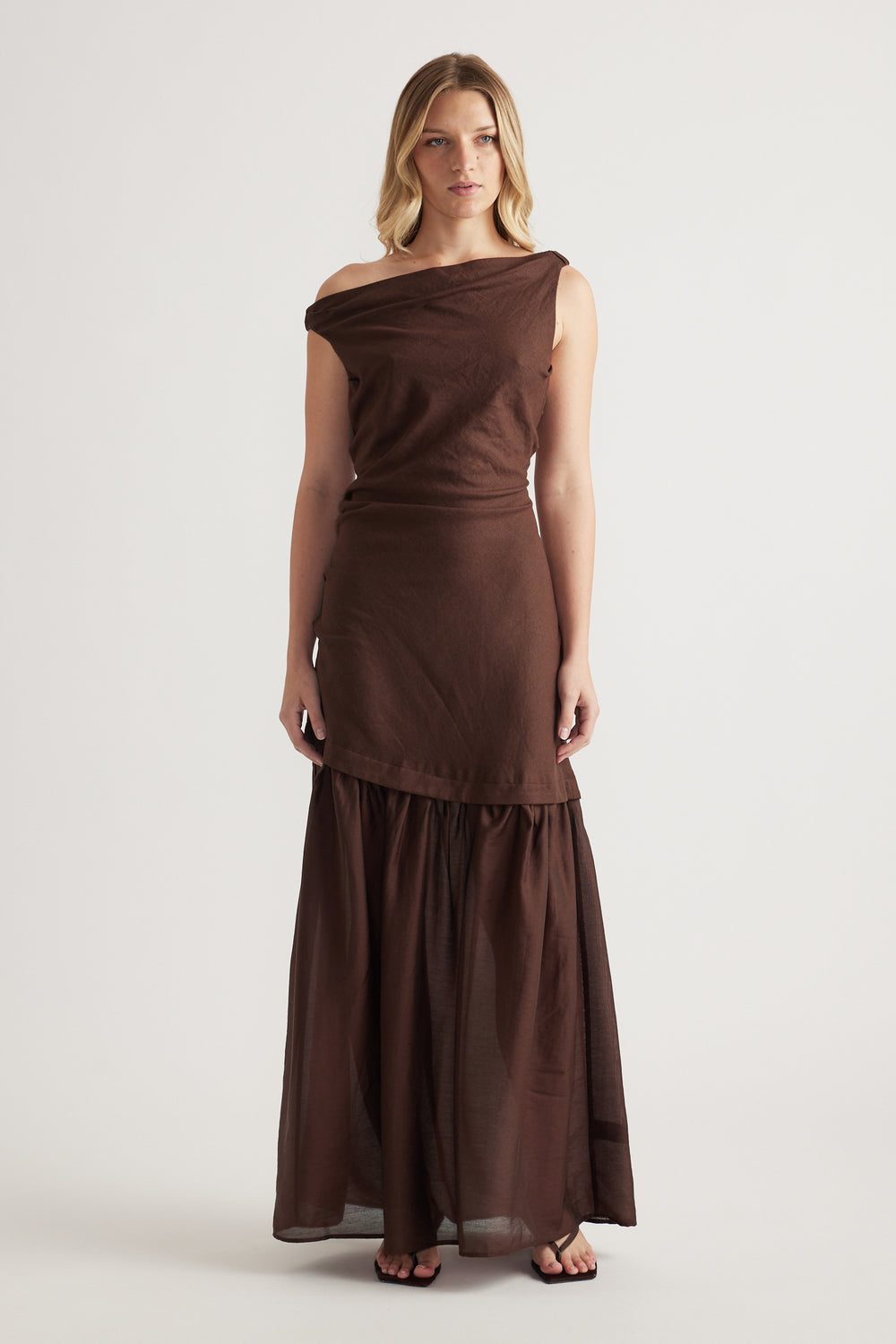 Woman wearing a brown off shoulder maxi dress with a draped bodice and flowing skirt