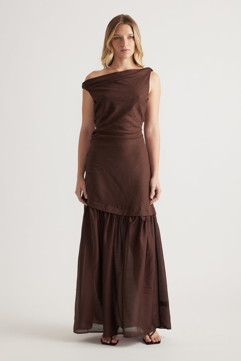 Woman wearing a brown off shoulder maxi dress with a draped bodice and flowing skirt