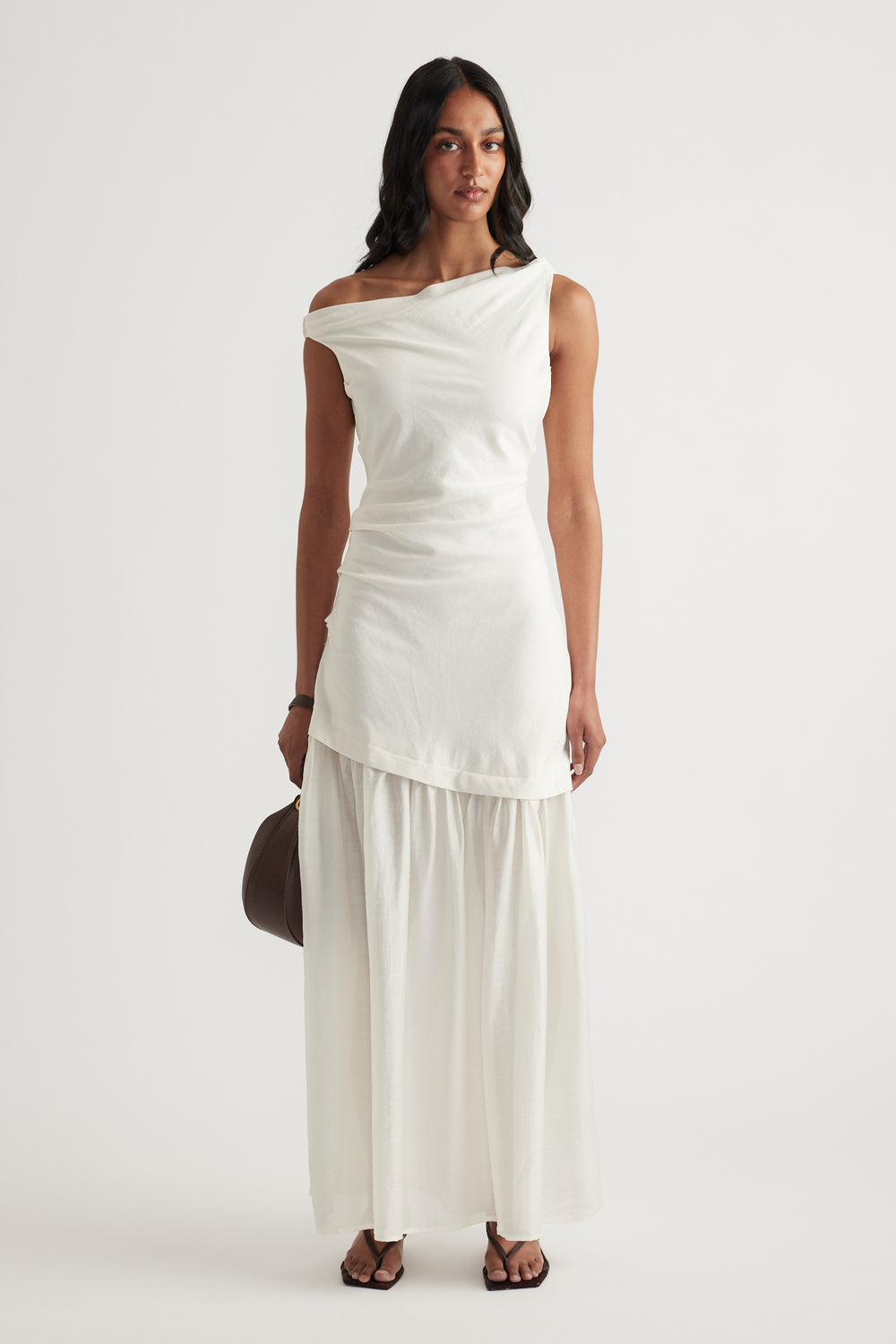 Woman wearing an off shoulder cream spliced maxi dress with a draped bodice and flowing skirt