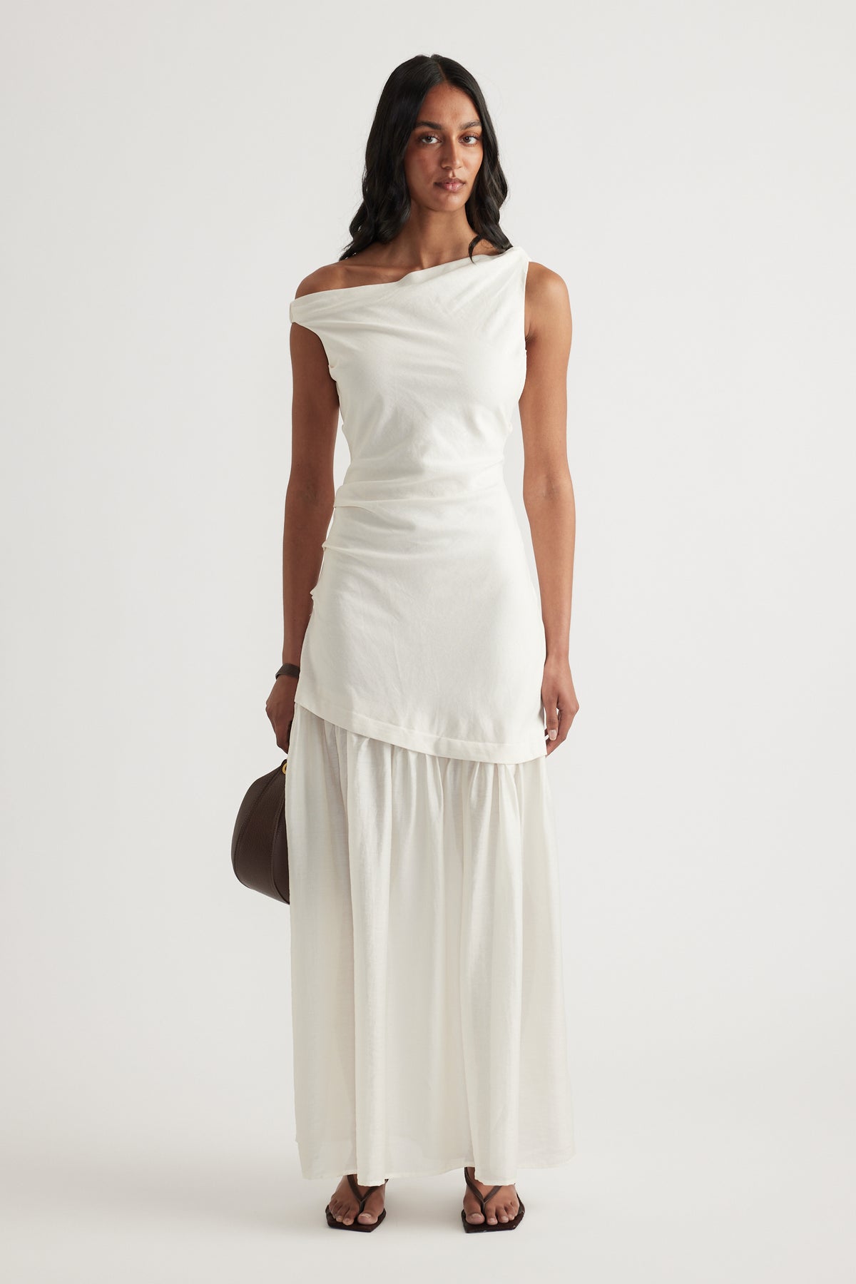 Woman wearing an off shoulder cream spliced maxi dress with a draped bodice and flowing skirt