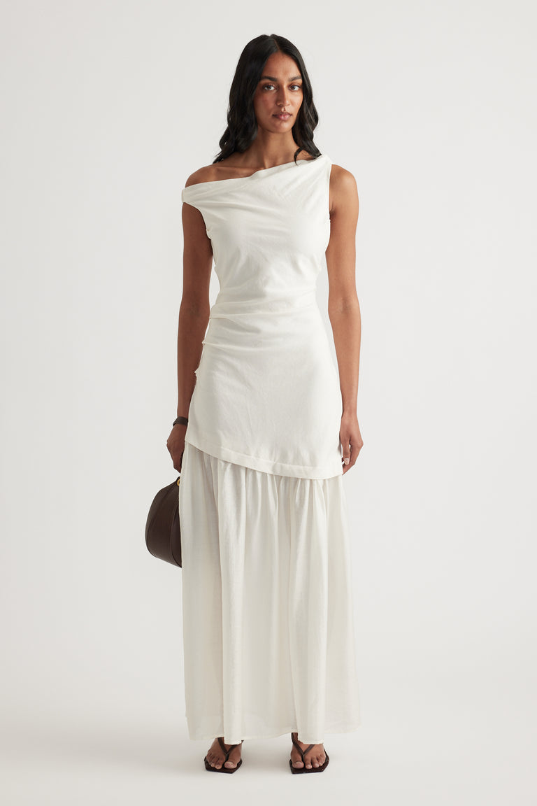 Woman wearing an off shoulder cream spliced maxi dress with a draped bodice and flowing skirt