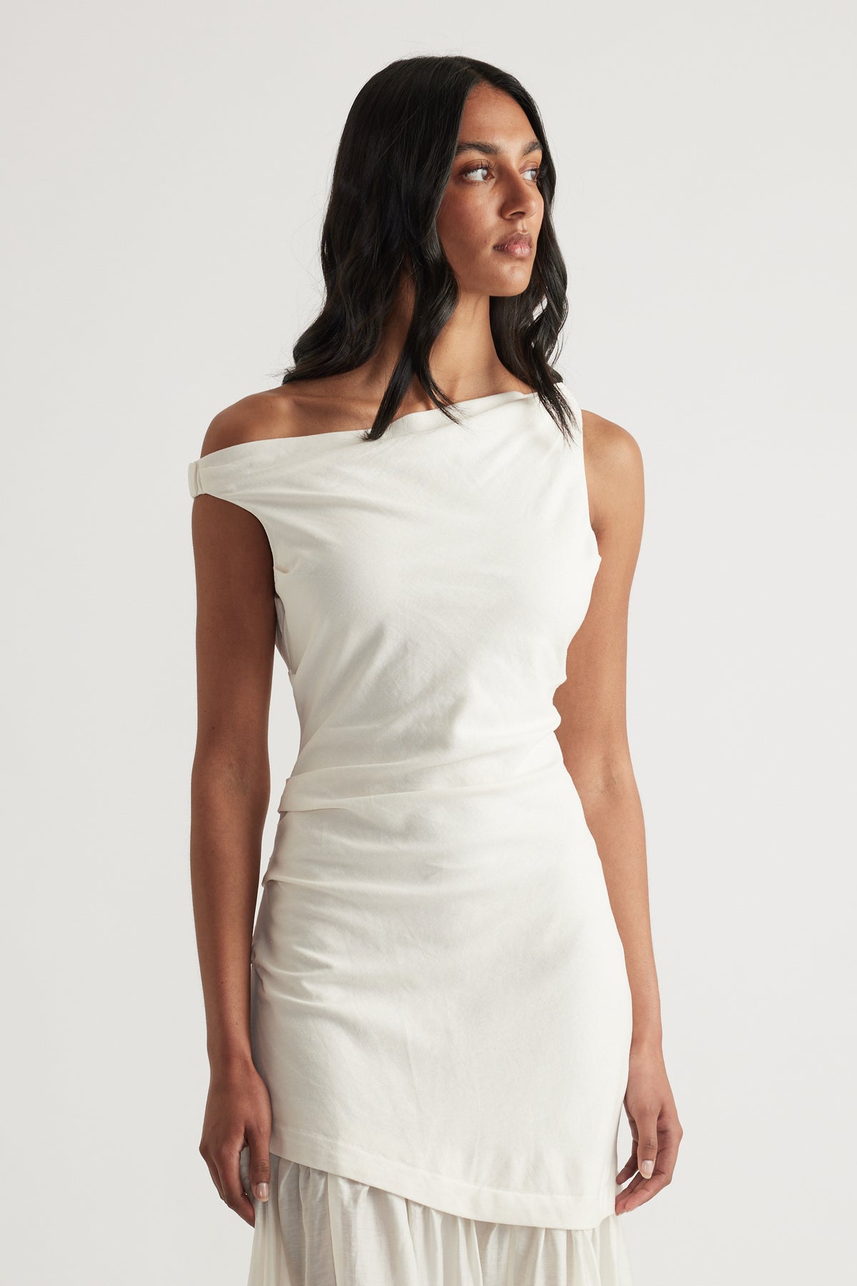 Woman wearing a white asymmetric off shoulder maxi dress with a fitted draped silhouette