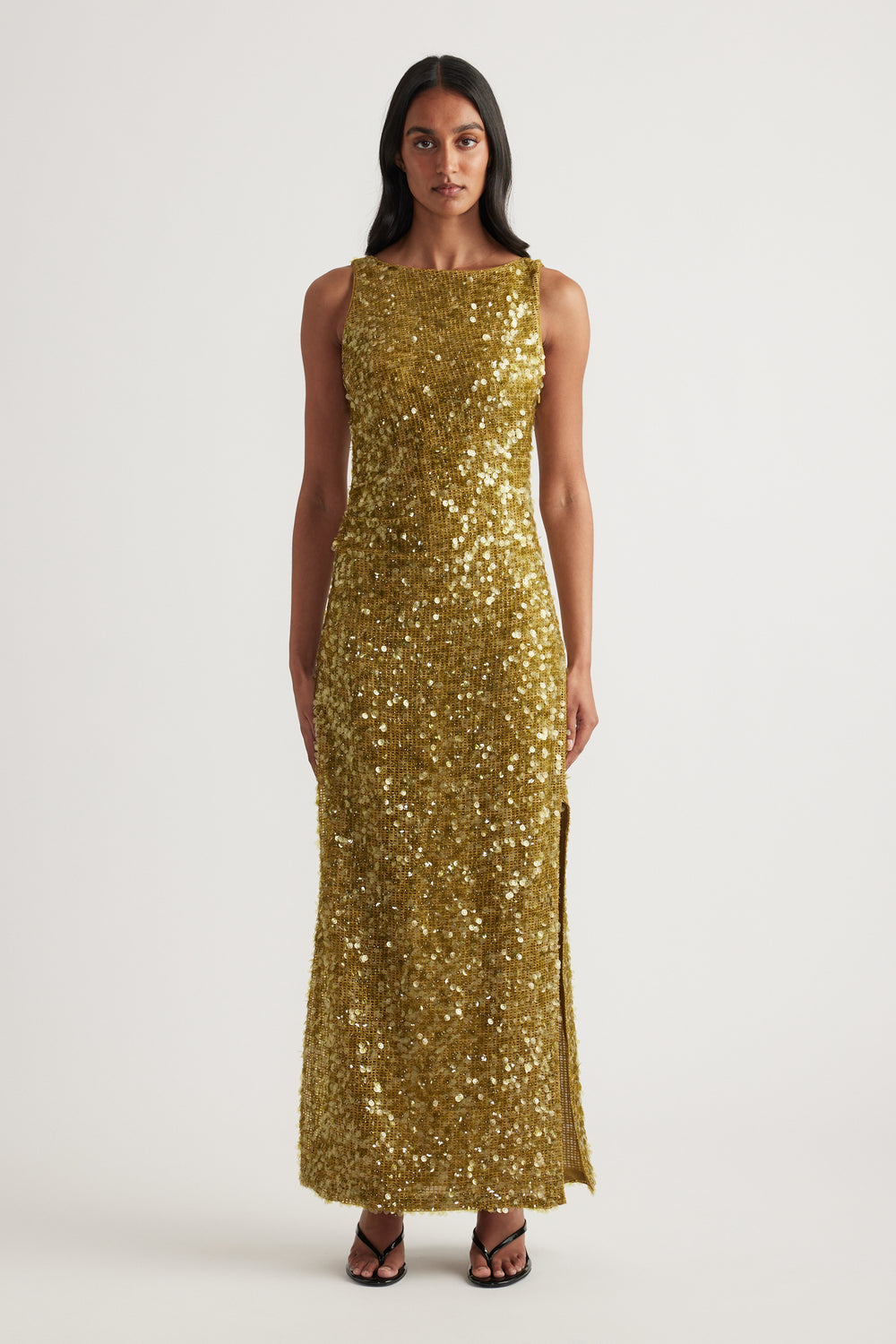 Woman wearing a gold sequin maxi dress with a sleeveless boat neckline and fitted silhouette