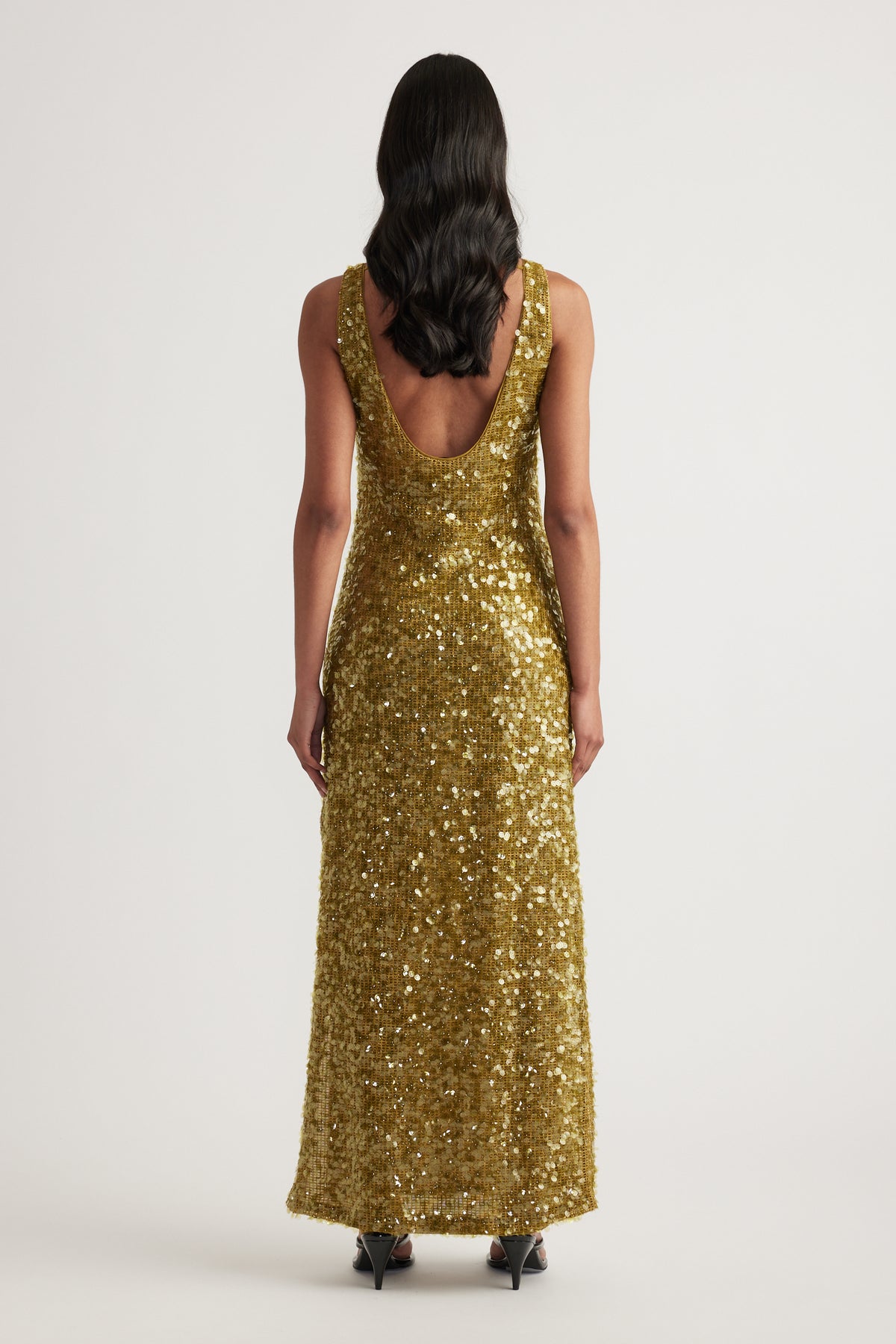 Woman viewed from behind in a gold sequin maxi dress with a scoop back and sleeveless silhouette