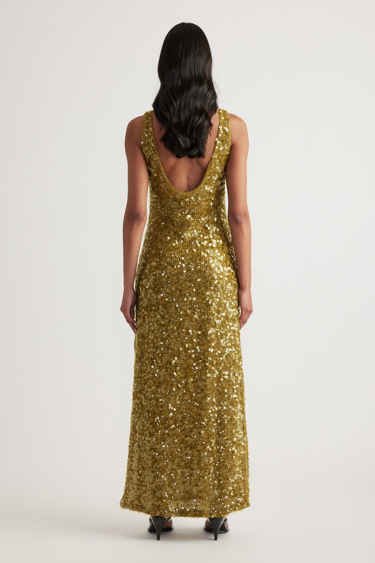 Woman viewed from behind in a gold sequin maxi dress with a scoop back and sleeveless silhouette