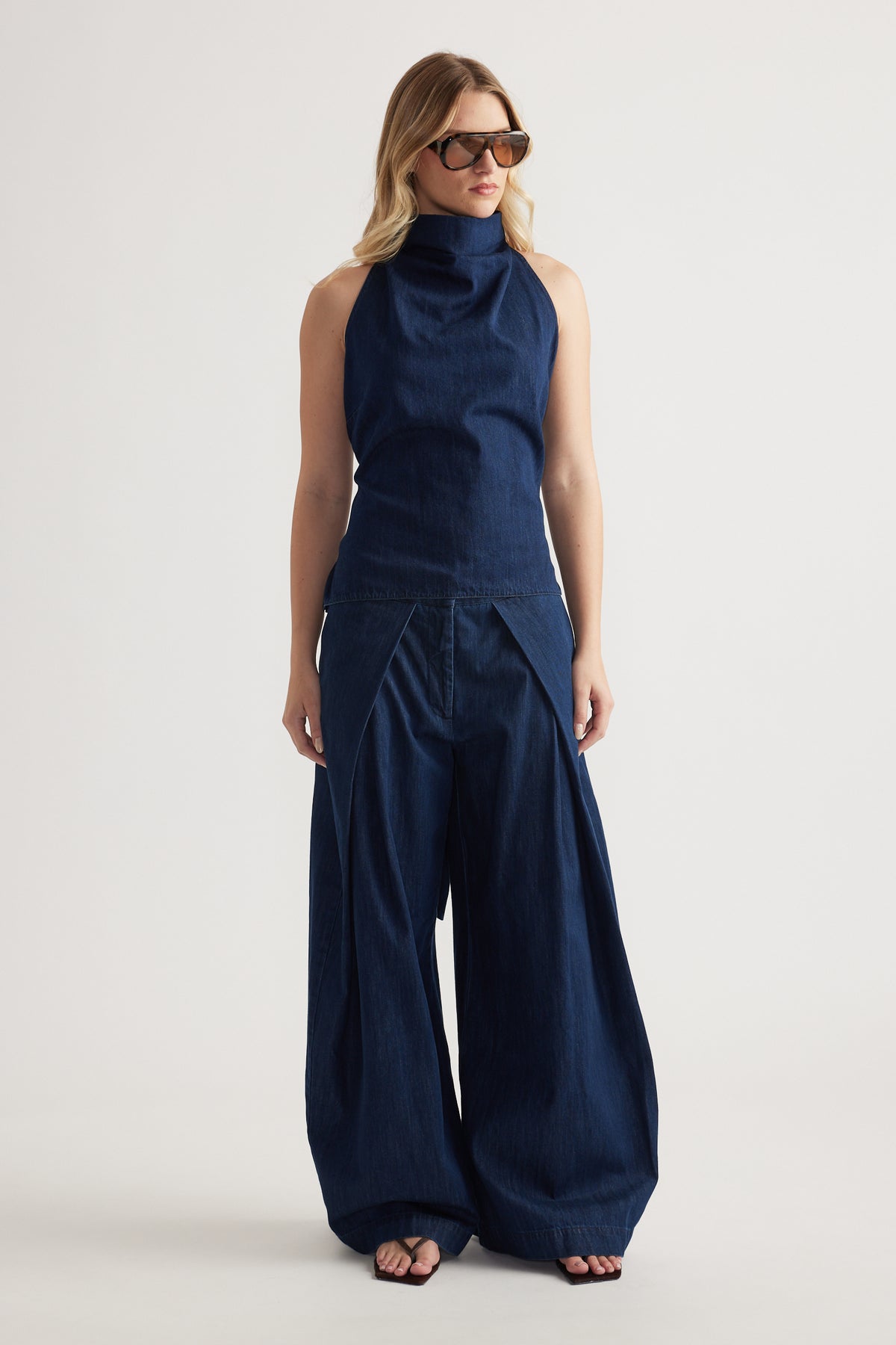 Woman wearing navy wide leg denim pants with a sleeveless high neck top and sunglasses