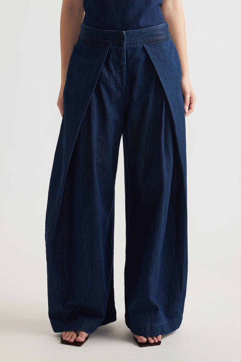 Woman wearing navy high rise wide leg pants with pleated waist and full length hems