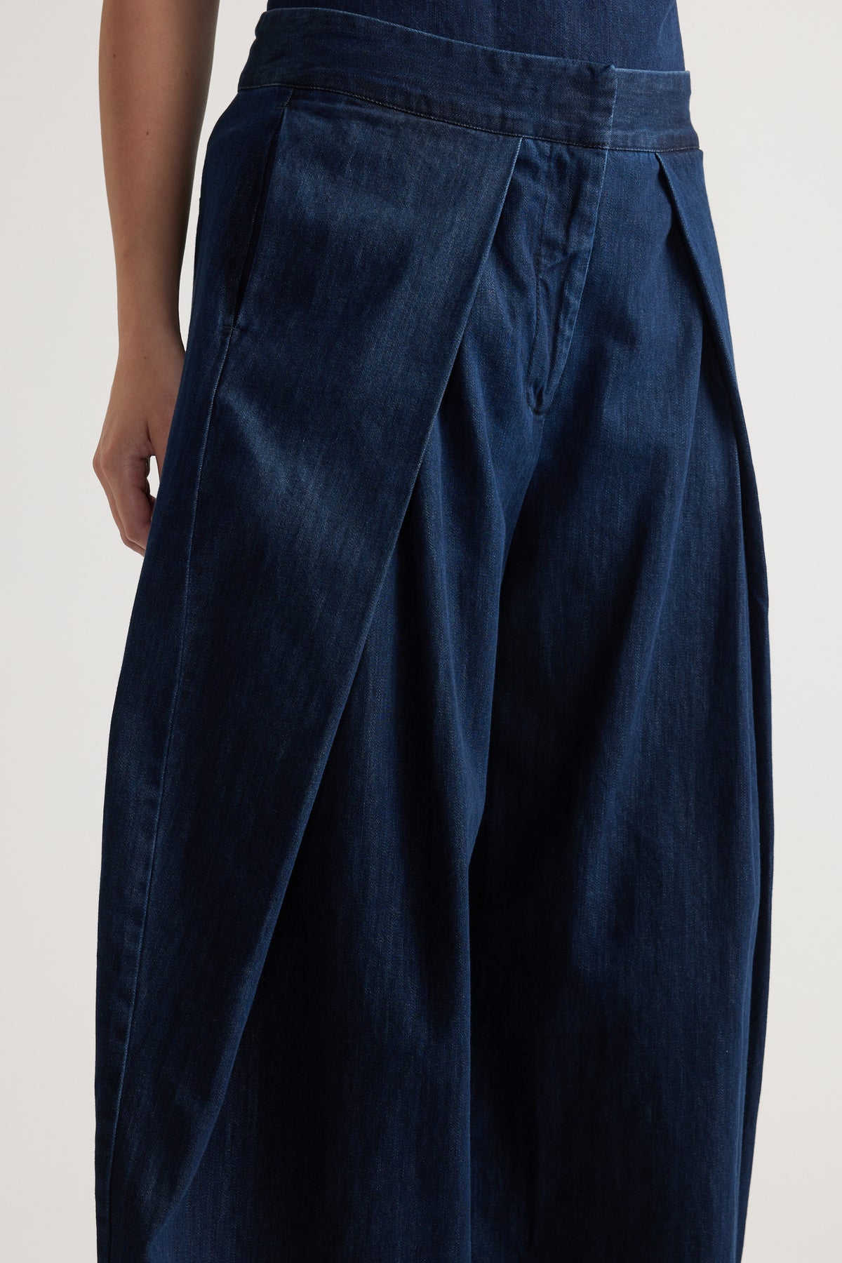 Model wearing dark denim high rise wide leg pants with pleated waist detail