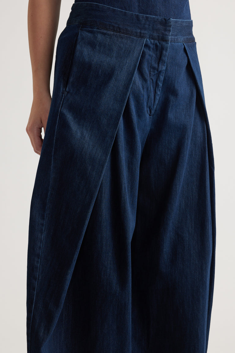 Model wearing dark denim high rise wide leg pants with pleated waist detail