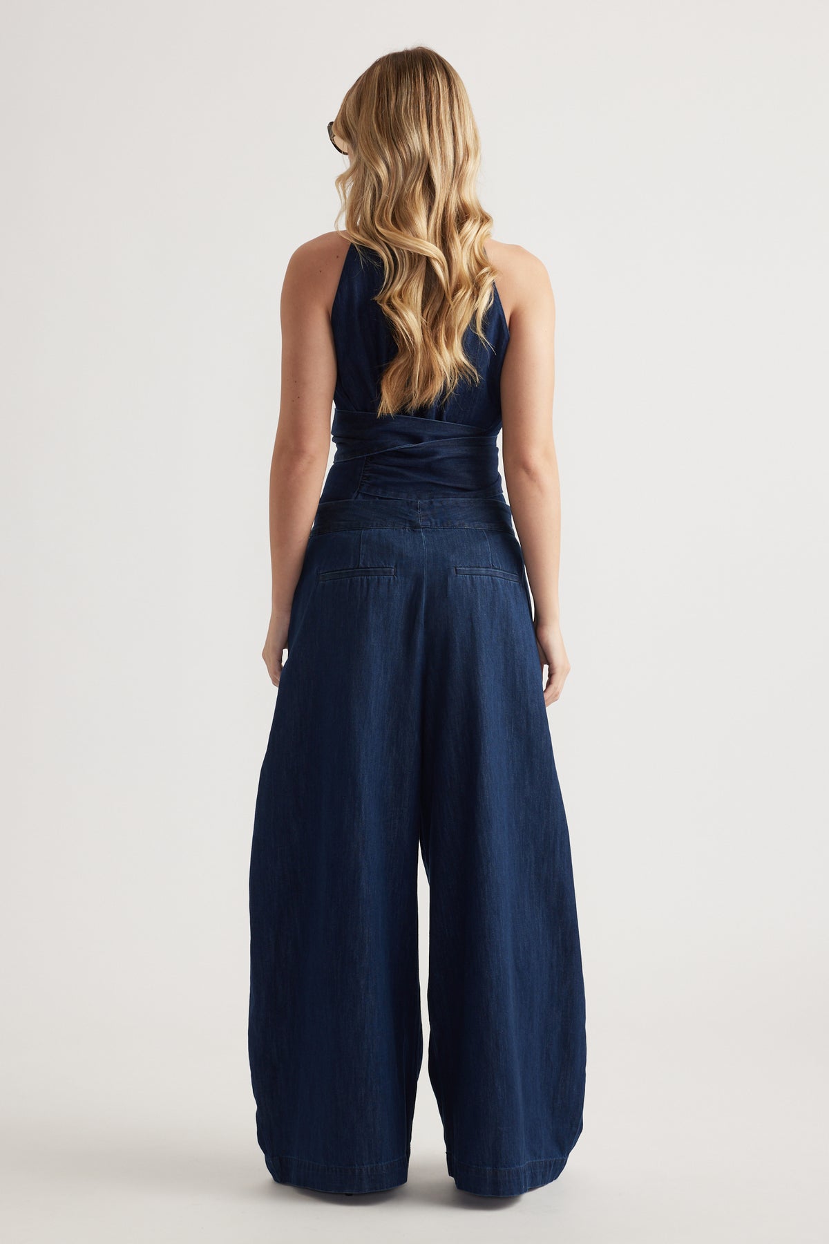 Back view of a woman wearing high-rise dark denim wide-leg pants with a sleeveless navy top