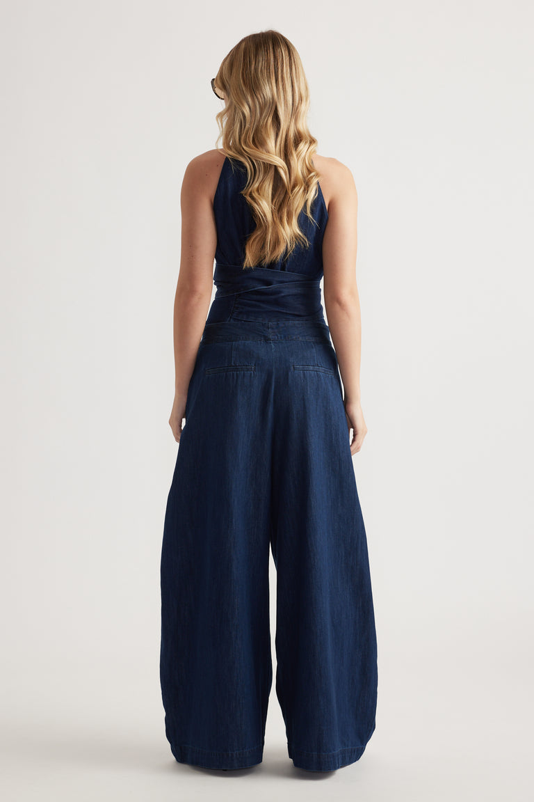 Back view of a woman wearing high-rise dark denim wide-leg pants with a sleeveless navy top