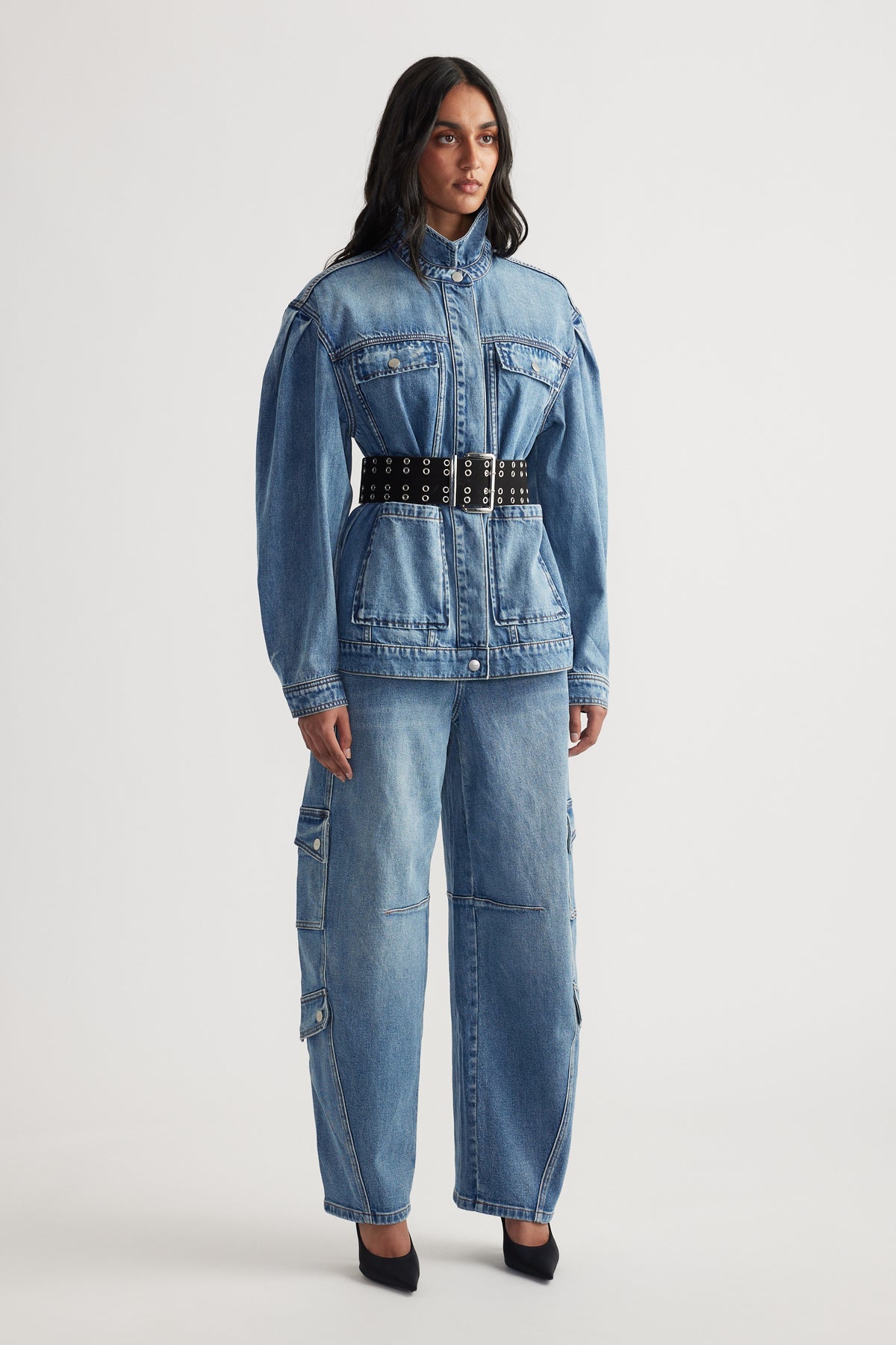Woman wearing belted denim jacket with puffed shoulders paired with loose-fitting cargo jeans and black pointed heels