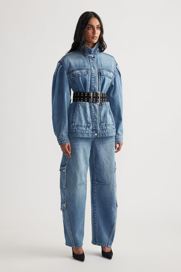 Woman wearing belted denim jacket with puffed shoulders paired with loose-fitting cargo jeans and black pointed heels
