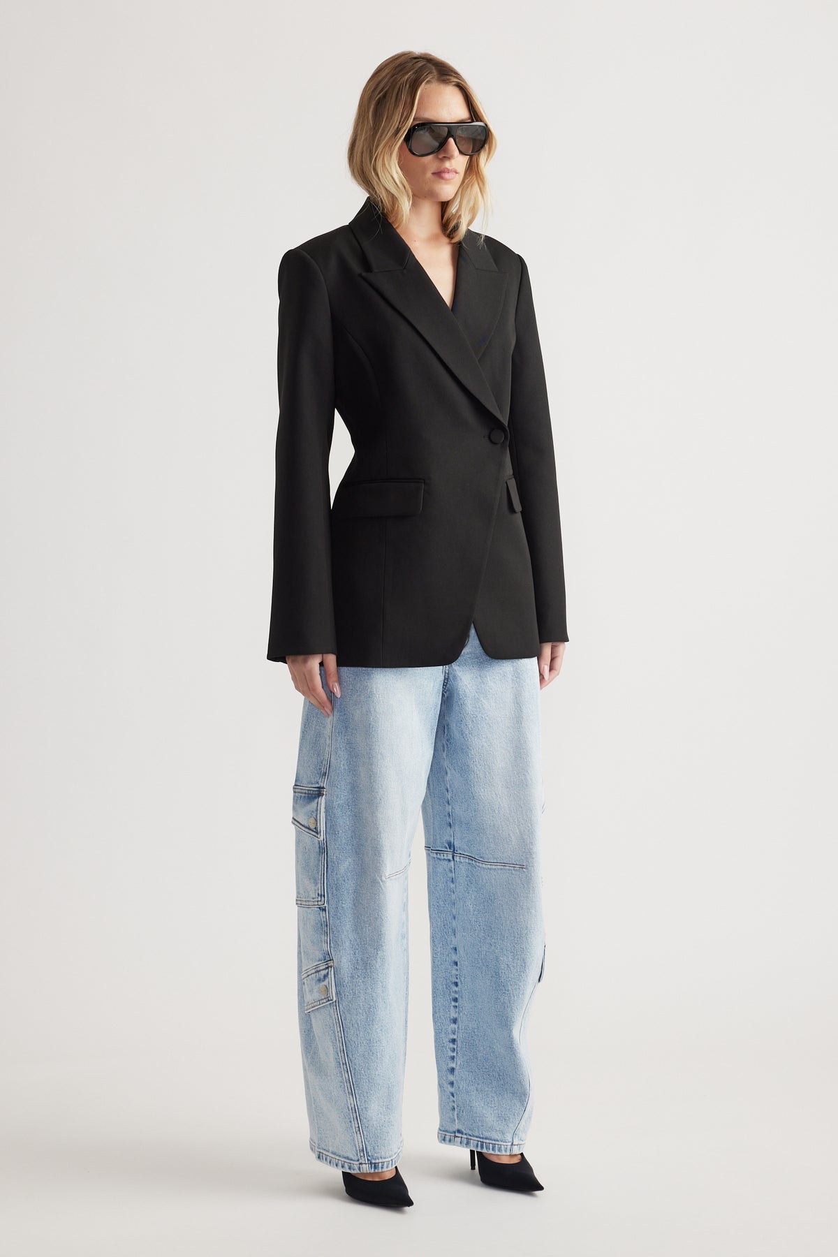 Woman wearing a black tailored blazer with wide-leg light wash cargo barrel jeans and black pointed heels