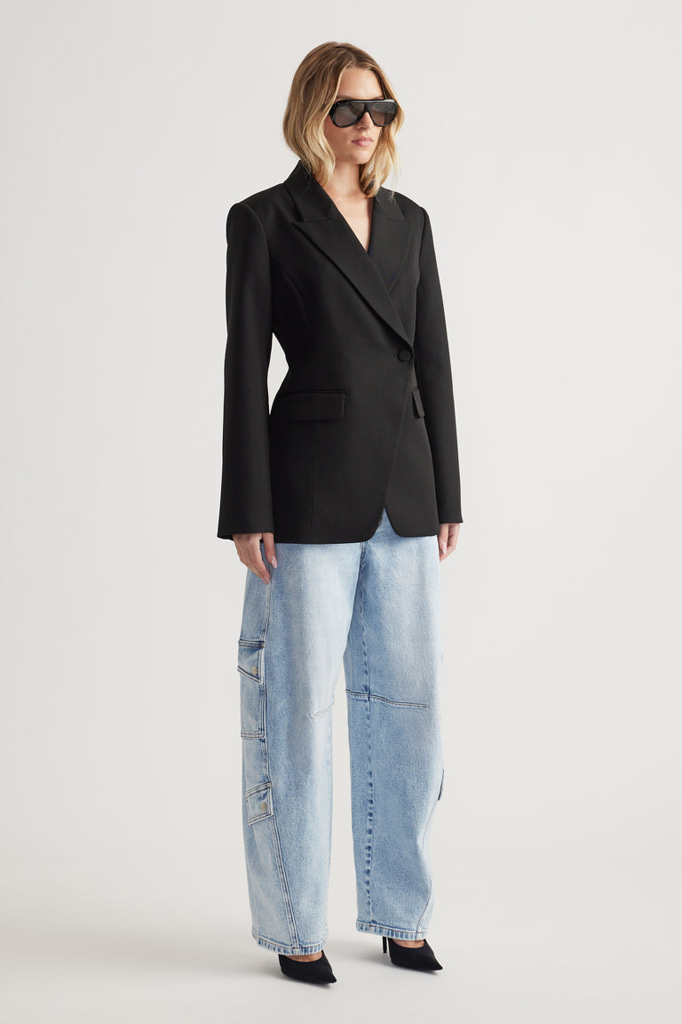 Woman wearing a black tailored blazer with wide-leg light wash cargo barrel jeans and black pointed heels