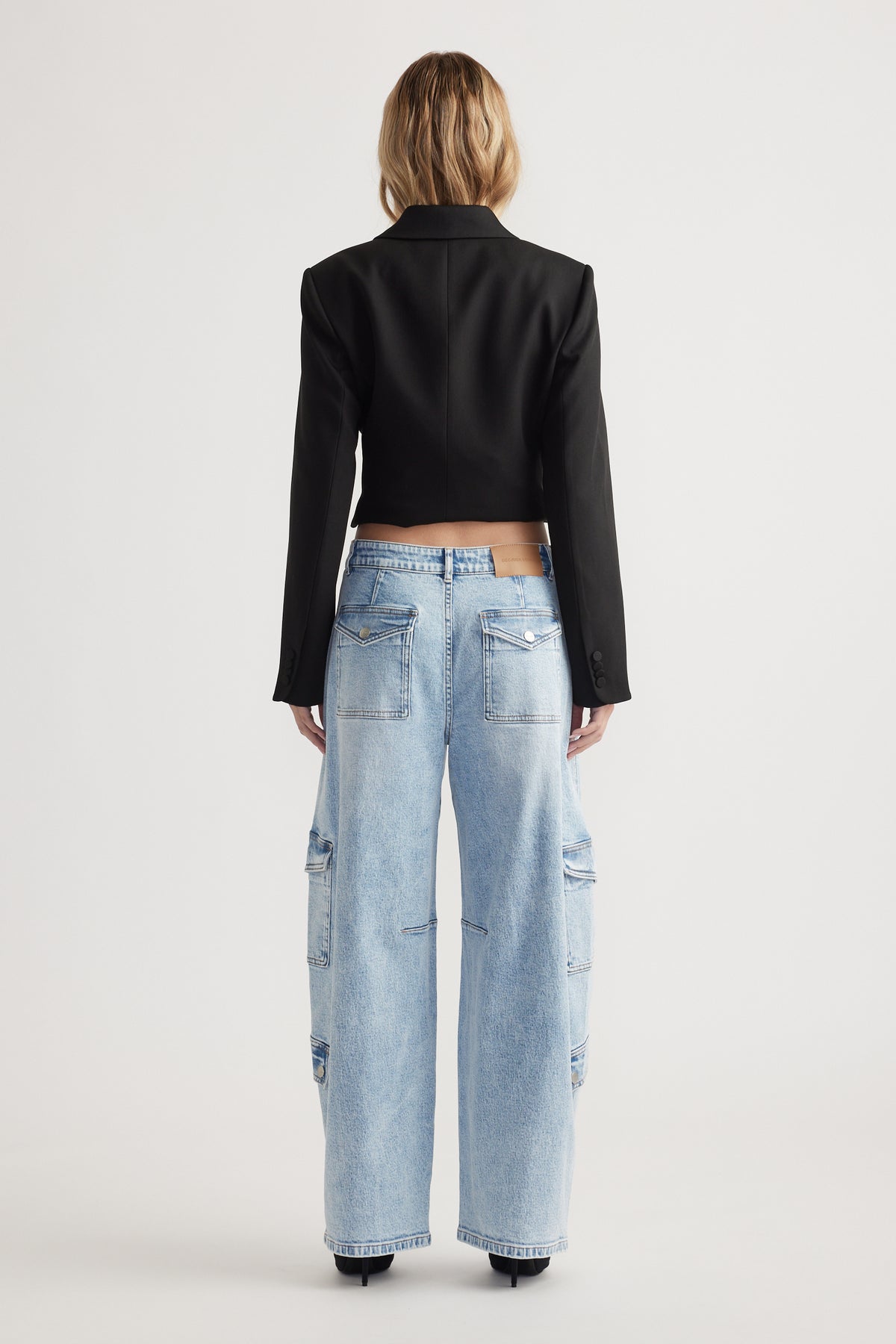 Rear view of light-wash wide-leg denim jeans with cargo pockets styled with a cropped black blazer and heels