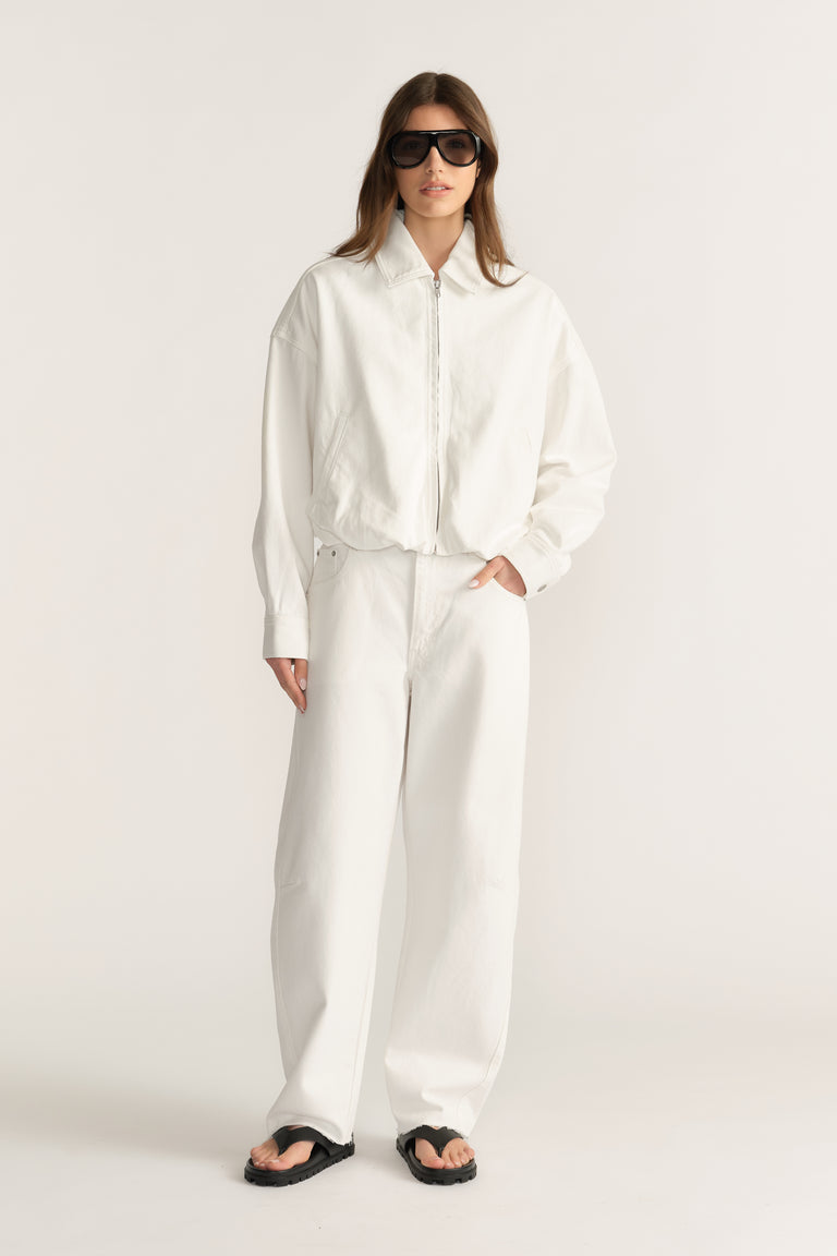 Woman wearing a white denim bomber jacket with wide leg pants, sunglasses and sandals