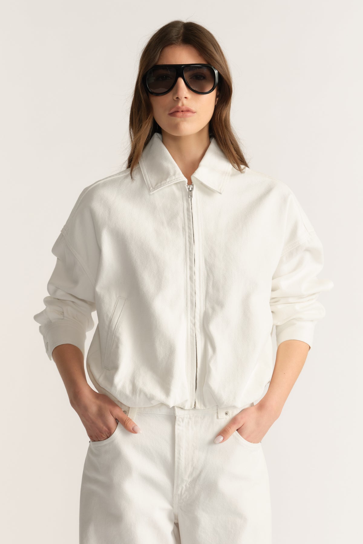 Woman wearing a white denim bomber jacket with matching jeans and oversized sunglasses
