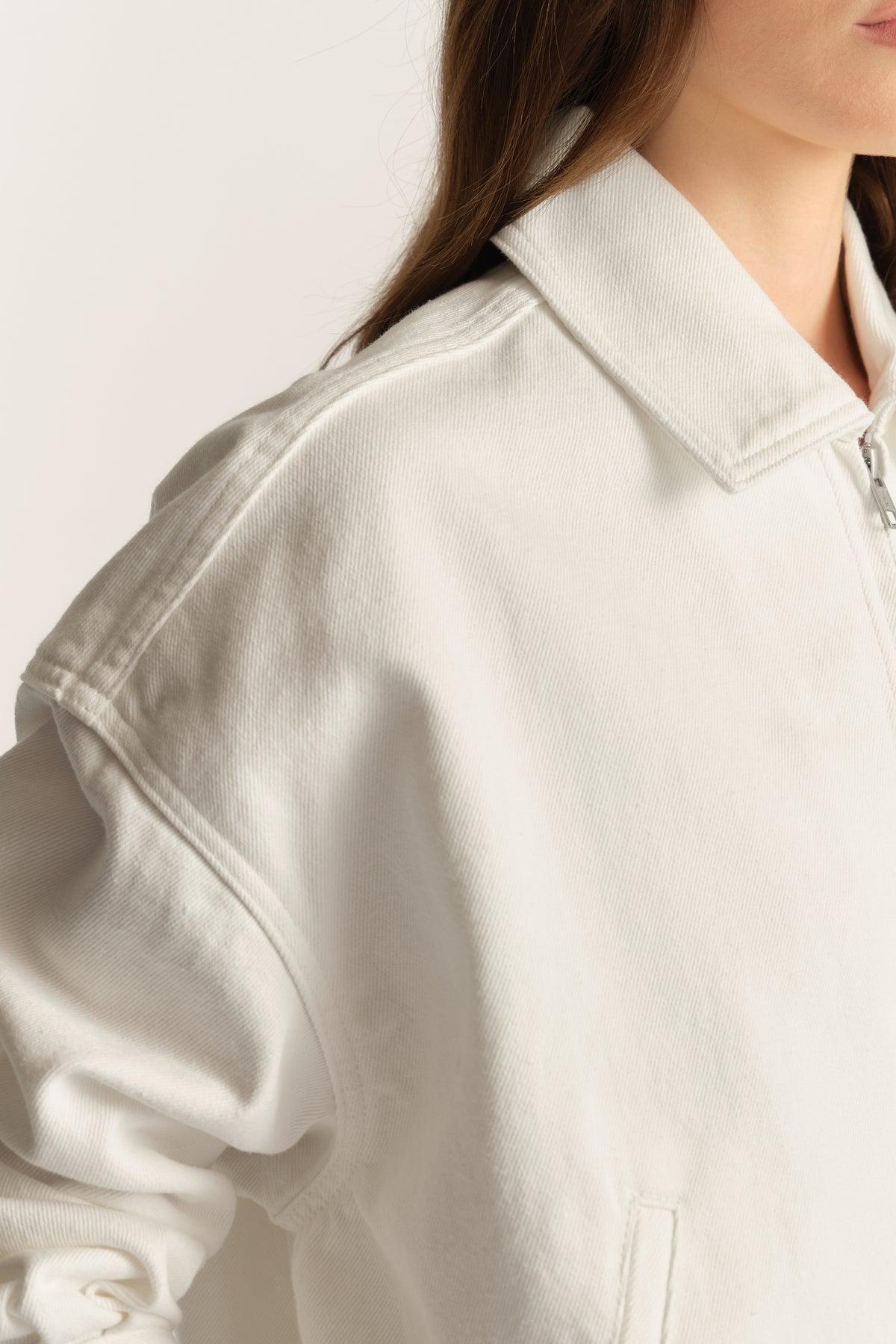 Woman wearing an off-white denim bomber jacket with a collared neckline and zip front