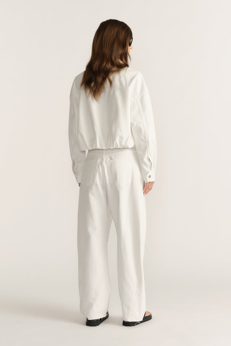Woman wearing a white cropped bomber jacket with an elasticated hem and matching wide-leg pants, viewed from behind
