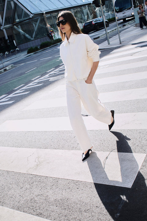 Woman wearing a white shirt and relaxed white barrel leg jeans with black slingback shoes crossing a city street