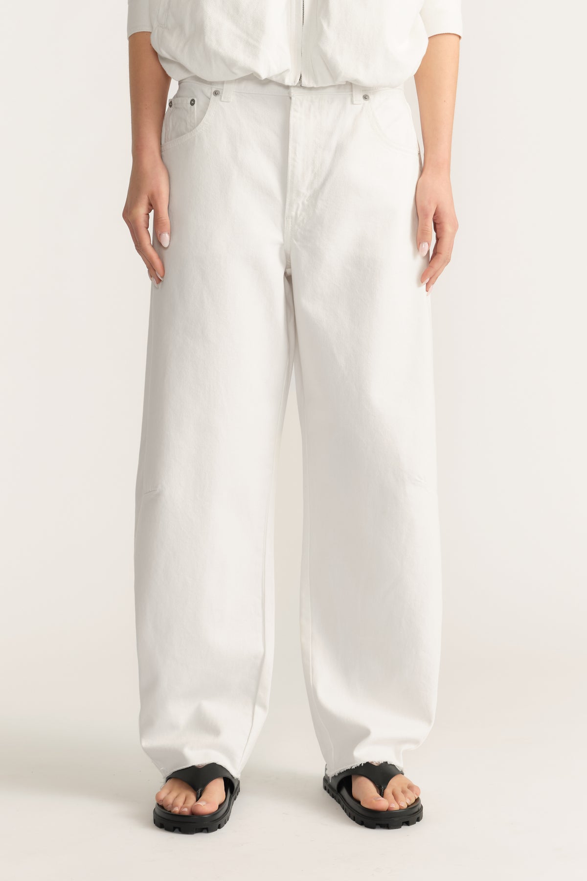 Woman wearing white barrel-leg jeans with a white top and black sandals
