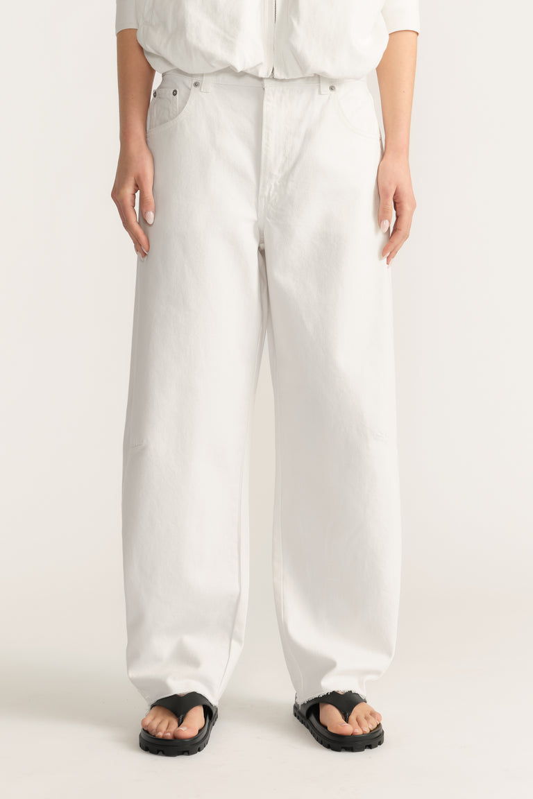 Woman wearing white barrel-leg jeans with a white top and black sandals