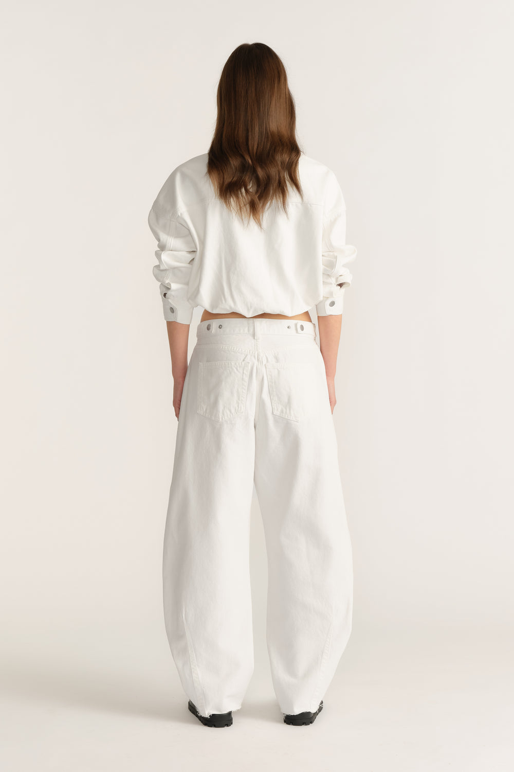Woman wearing white barrel-leg jeans with a cinched waist and cropped long-sleeve top, viewed from behind