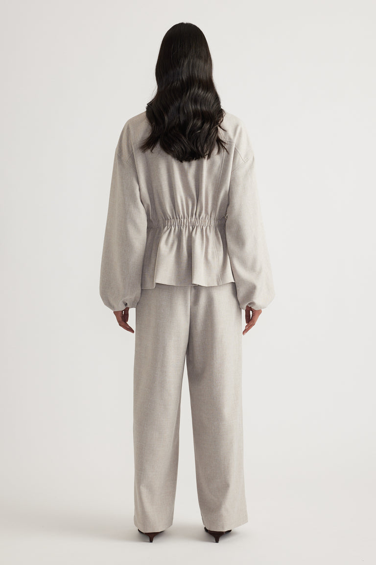 Back view of a woman wearing a beige cinched waist jacket with matching wide leg pants and black heels