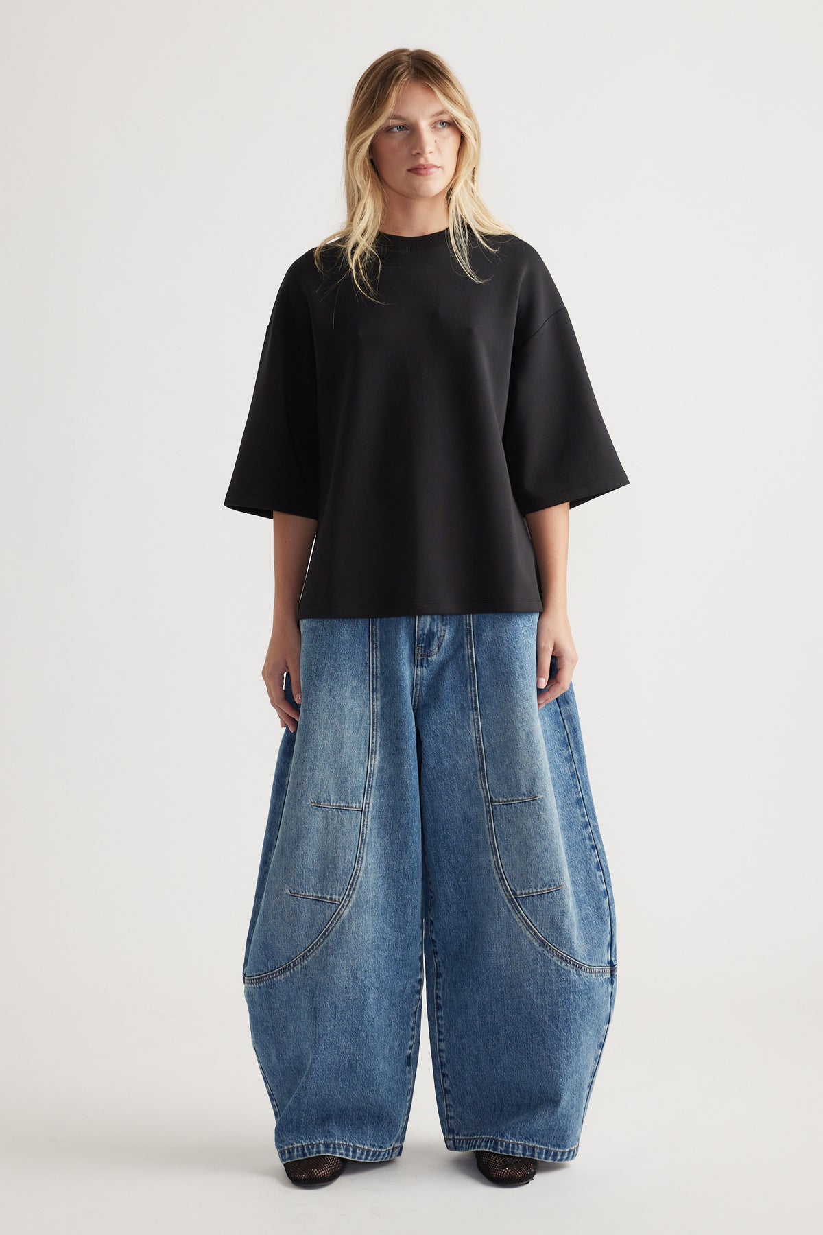 Woman wearing oversized black short sleeve top with crew neck paired with wide-leg blue denim pants