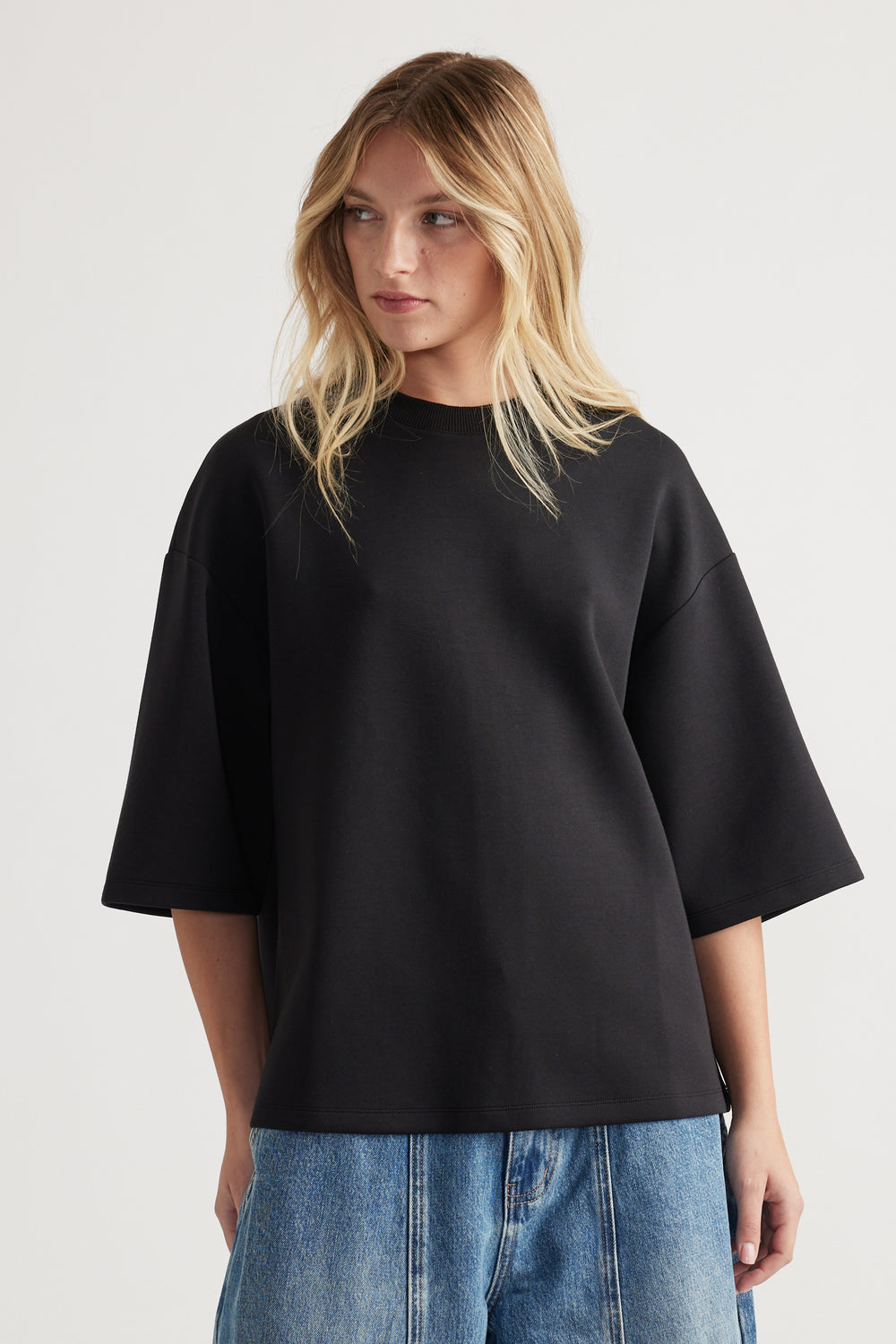 Woman wearing an oversized black short sleeve tee with crew neck paired with loose light blue denim jeans