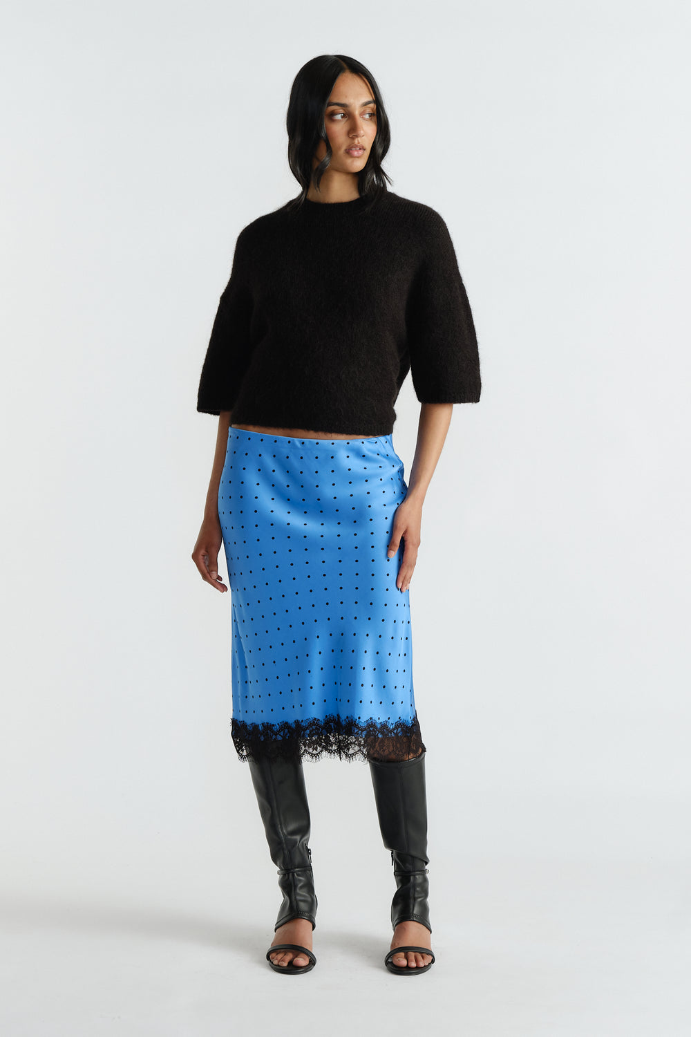 Woman wearing a soft black cropped sweater paired with a blue midi skirt featuring black lace trim and spots.