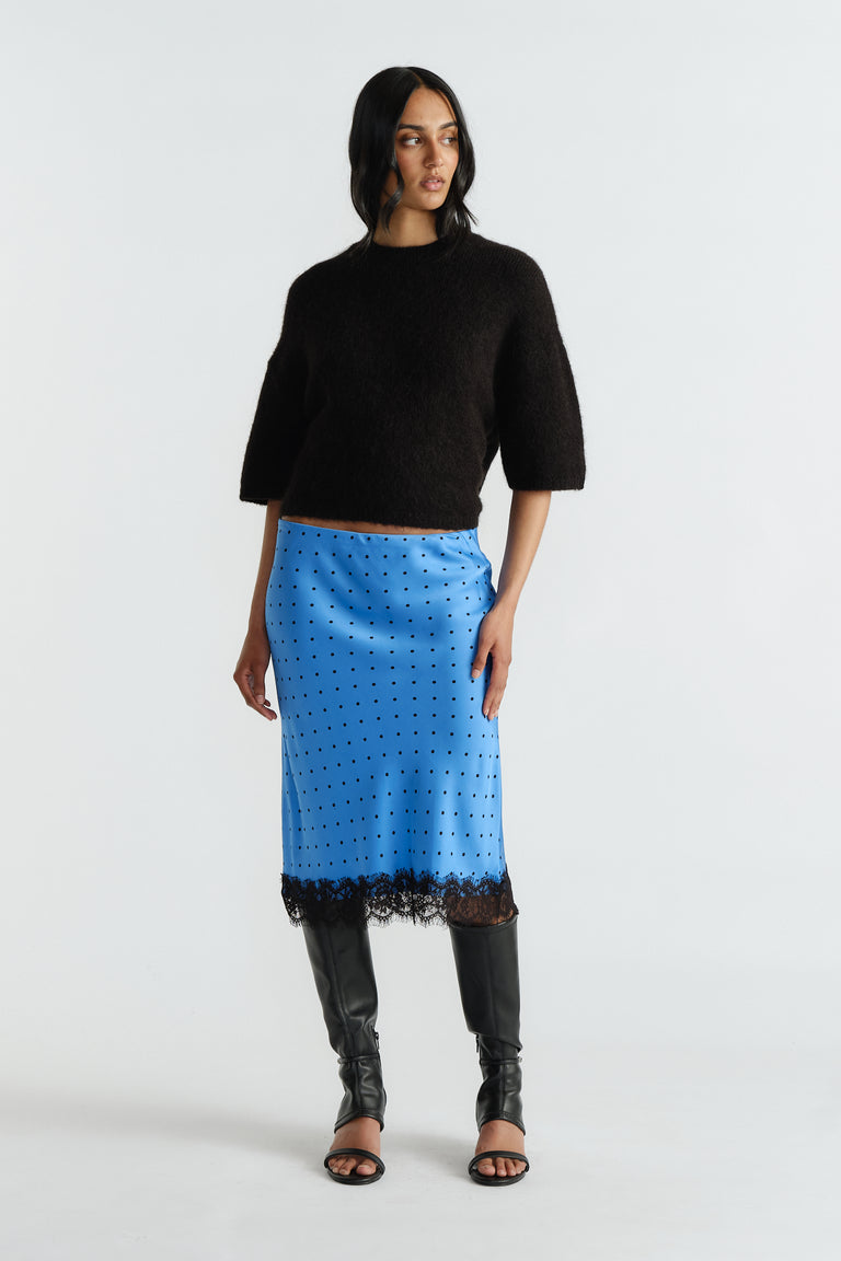 Woman wearing a soft black cropped sweater paired with a blue midi skirt featuring black lace trim and spots.