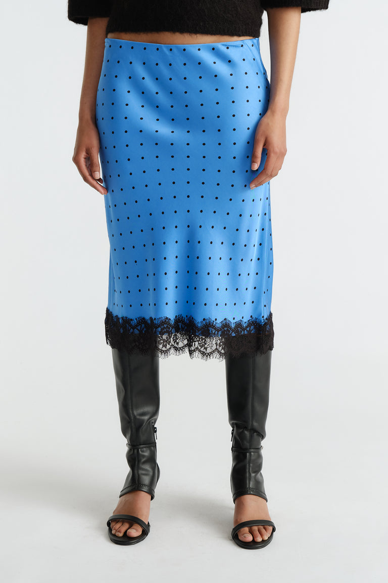 Blue midi skirt with black polka dots and lace trim, styled with black open-toe heels and tall boots.