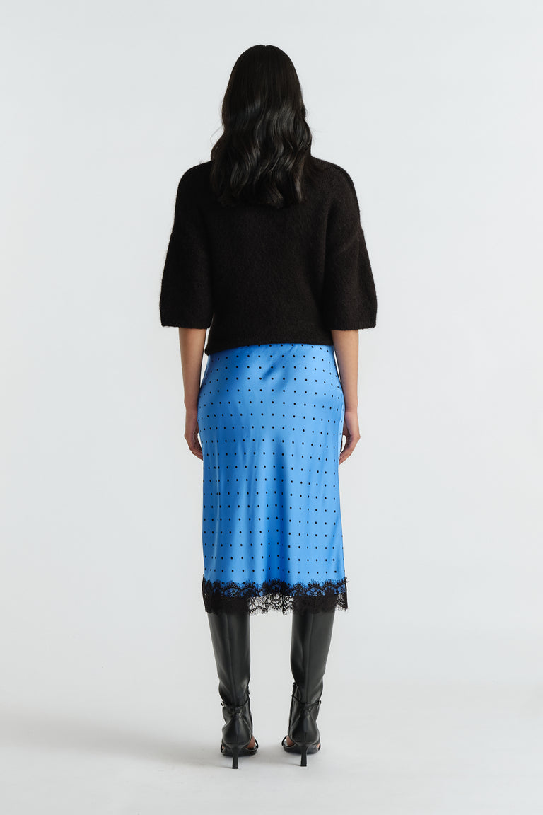 Woman wearing a bright blue midi skirt with black polka dots and lace trim, styled with a black top and boots.