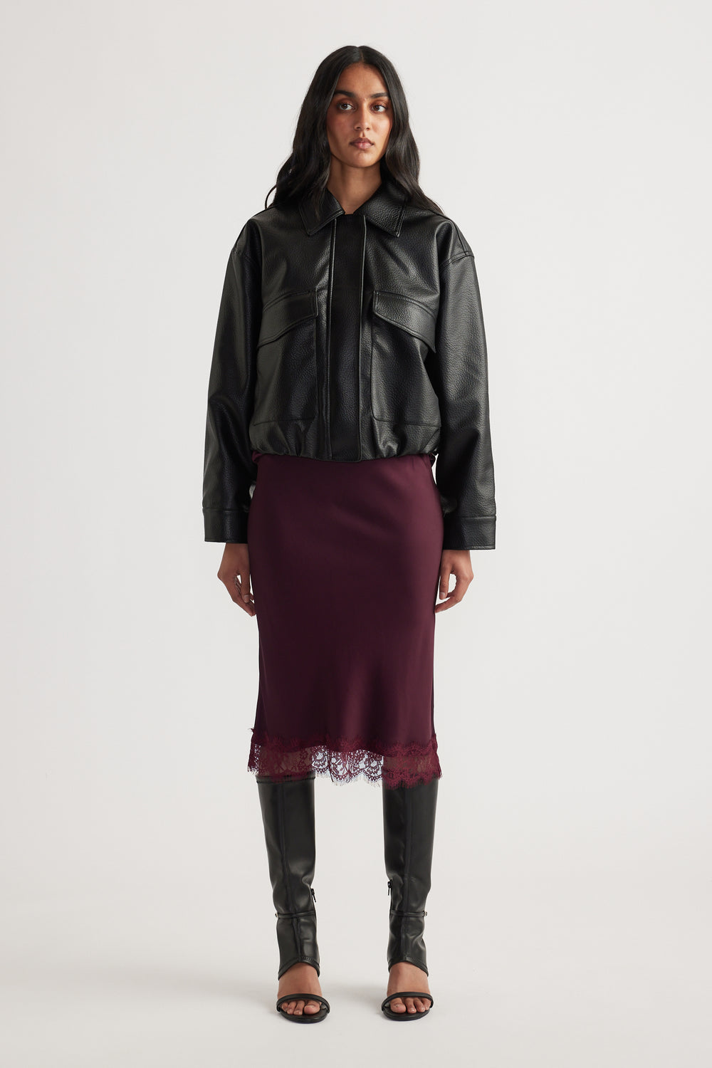 Woman wearing a burgundy lace-trim midi skirt with a black leather jacket and tall black boots